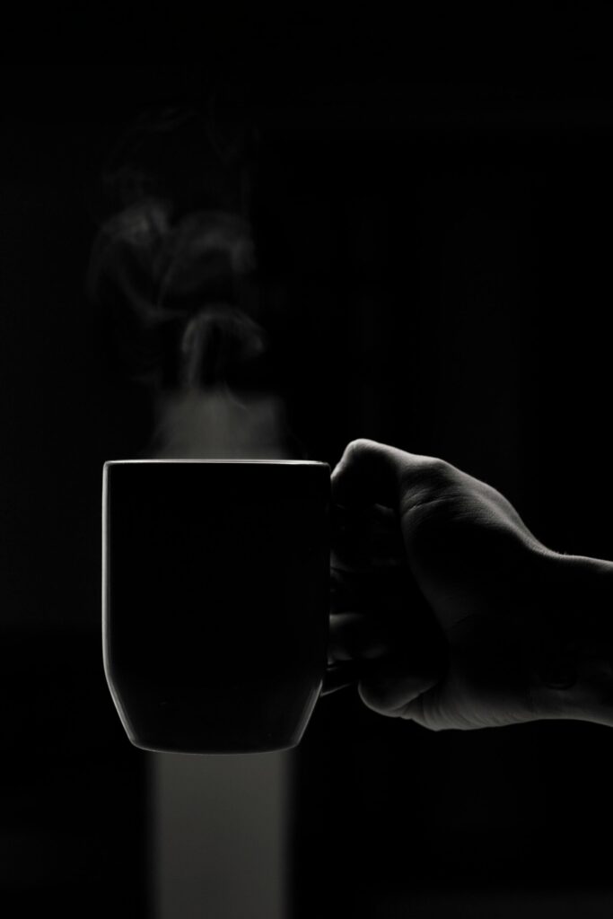 Artistic shot of a hand holding a steaming mug in monochrome, conveying warmth and simplicity.