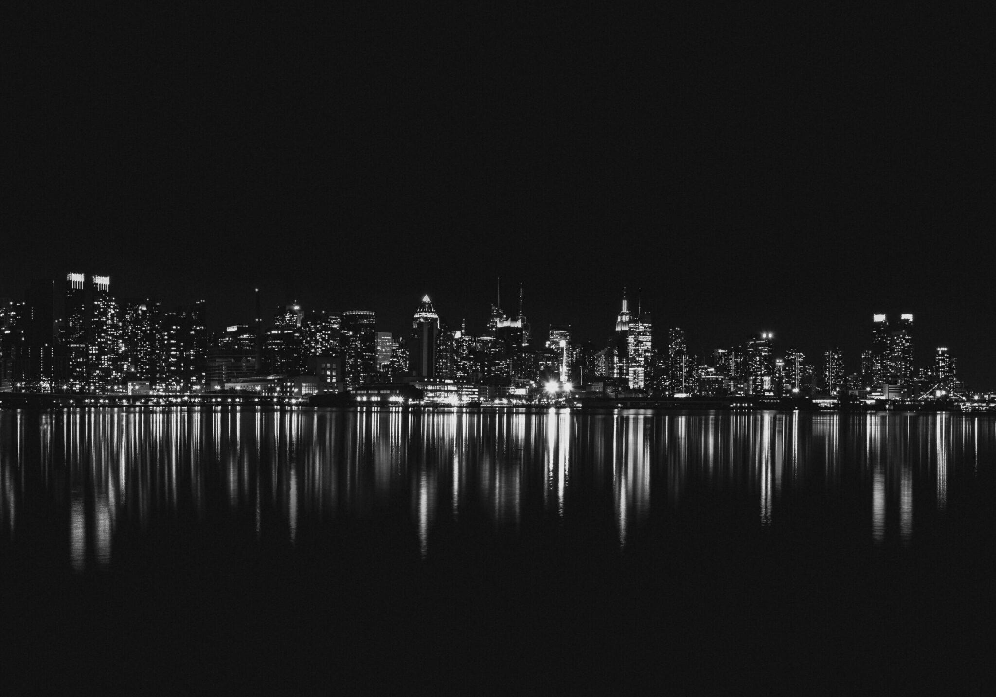 Captivating black and white view of New York City skyline reflecting on water at night.